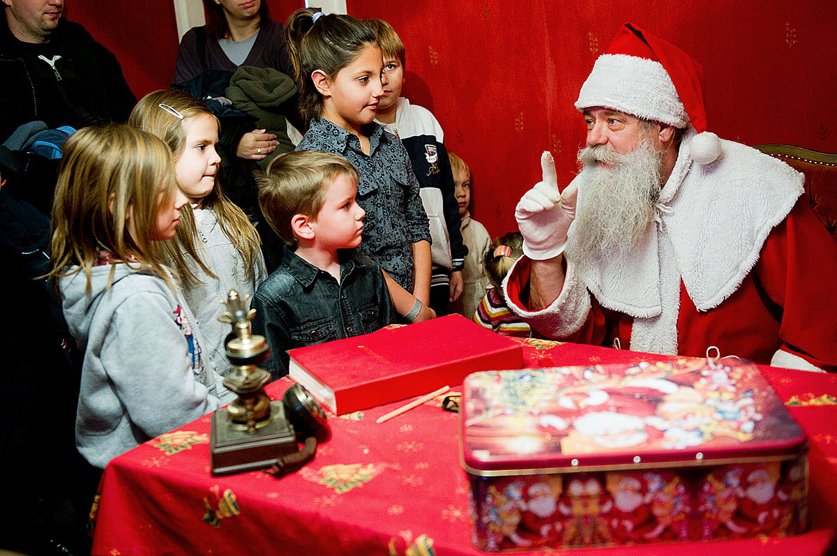 Gyerekekkel beszélget a Mikulás Nagykarácsony településen. A helyi postahivatalban ünnepi pecsétet nyomnak a következő hetekben