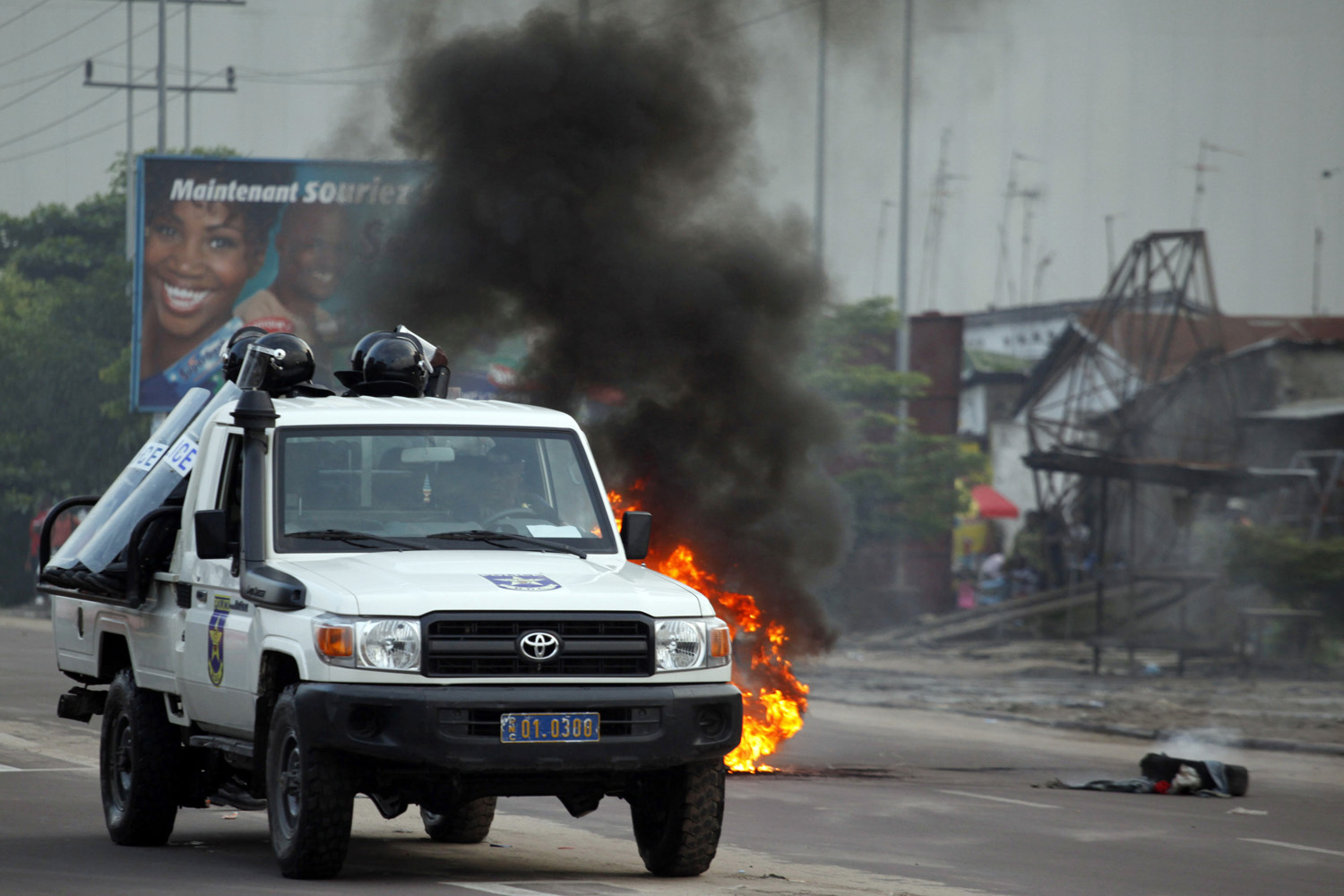 Pajzzsal védik magukat a rendőrautó nyitott platóján ülő kongói kommandósok, ahogy Kinshasa egyik utcáján hajtanak végig