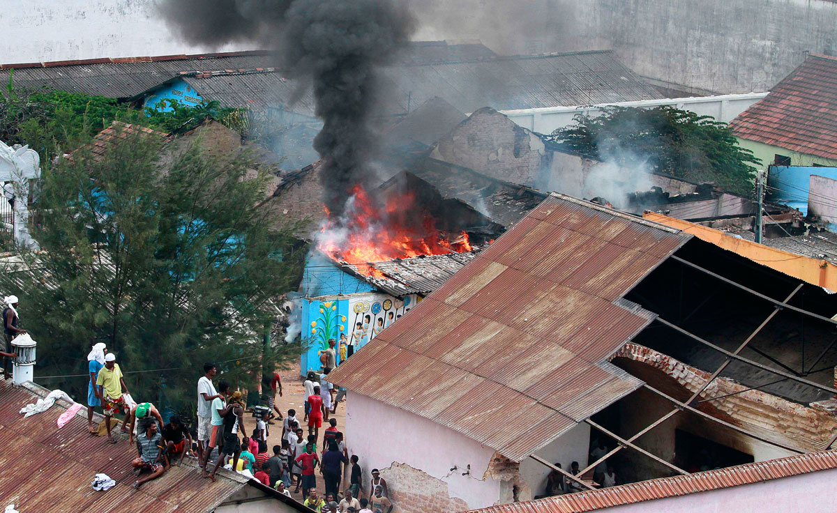 A Welikada börtön rabjai a tetőn állva nézik, amint társaik felgyújtják az épületet