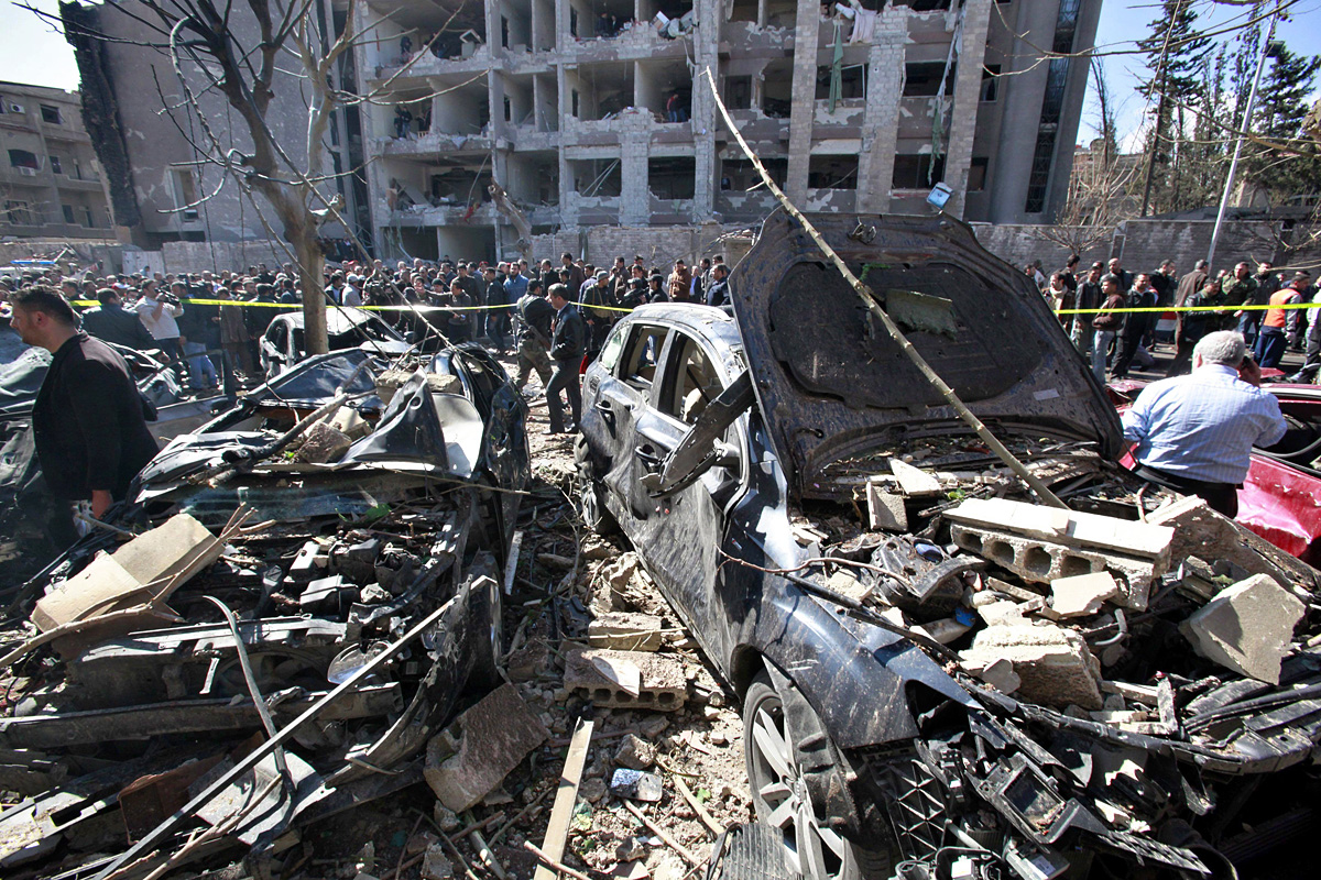 Súlyosan megrongálódott épületek és megsemmisült járművek az egyik robbanás helyszínén a szíriai fővárosban