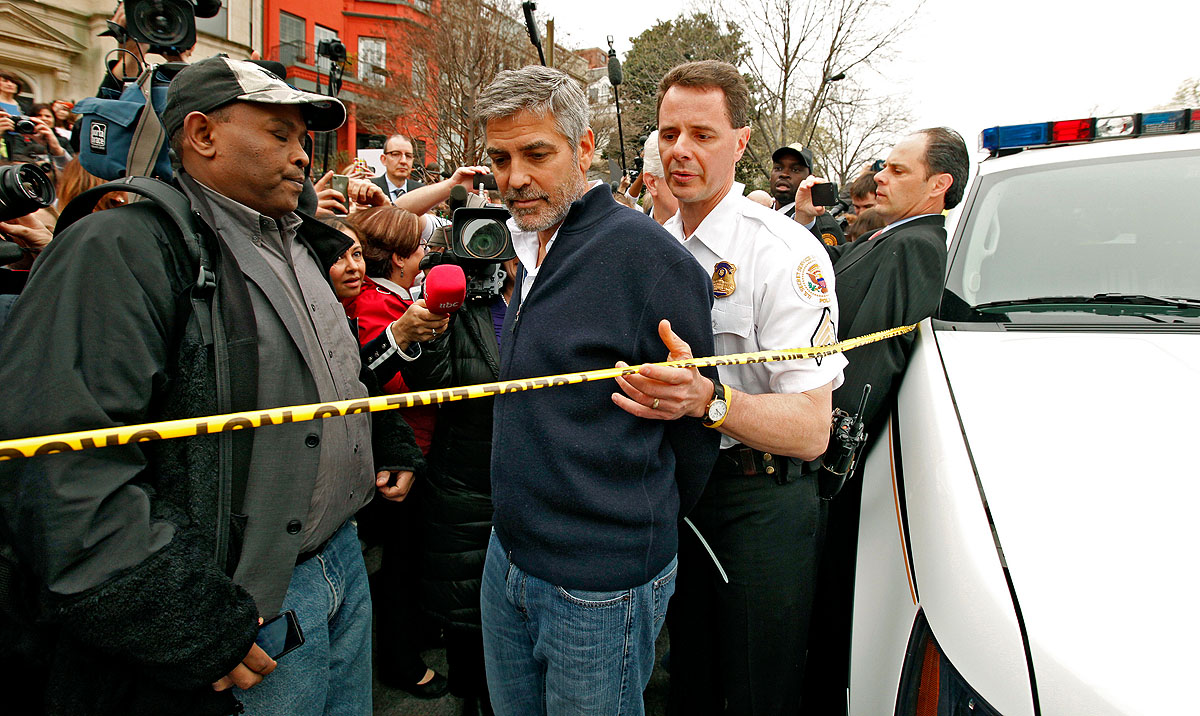A rendőrautóhoz kísérik a műanyag szorítóval megbilincselt George Clooney-t, akit polgári engedetlenség miatt Szudán washingtoni nagykövetsége előtt vettek őrizetbe