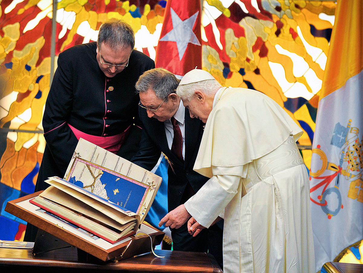 Raul Castro az ajándékba kapott könyvet nézi XVI. Benedek pápával a havannai forradalmi palotában