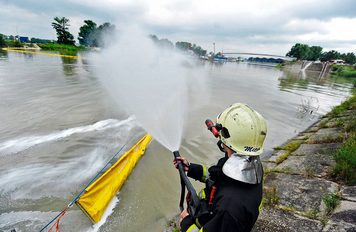 Egy tűzoltó próbálja megakadályozni a szennyeződés továbbterjedését a Dunán 