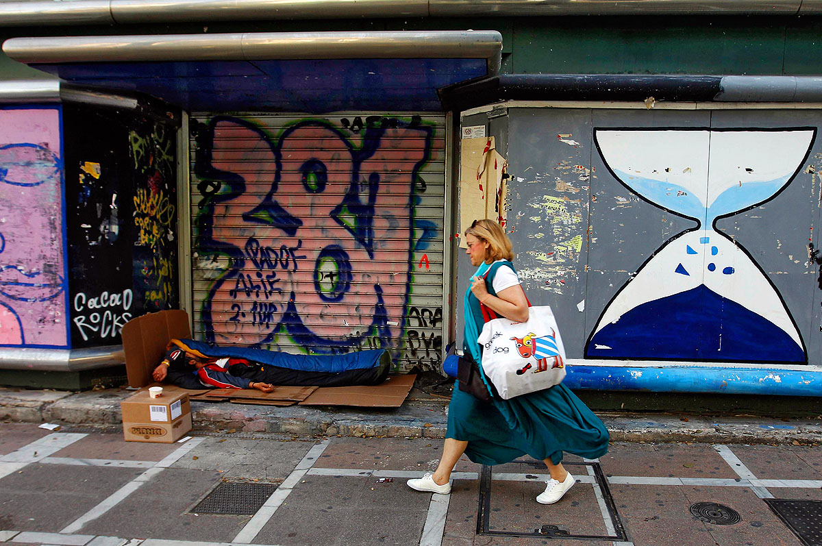 Bezárt üzlet bejárata előtt fekszik egy hajléktalan Athén belvárosában
