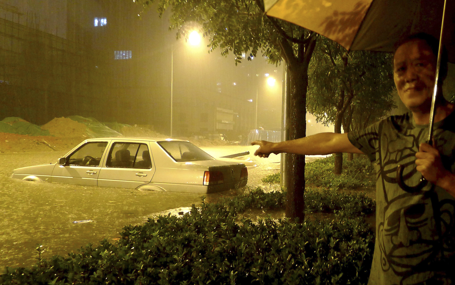 Egy pekingi férfi mutatja az özönvíz jellegű eső által elárasztott kocsiját