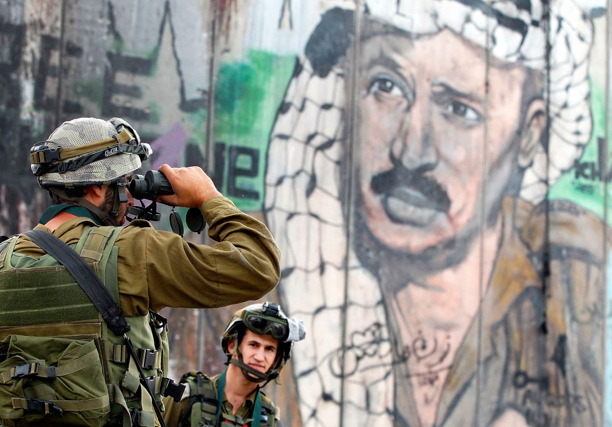 Izraeli katona távcsővel, az elhunyt palesztin vezető, Arafat képe előtt