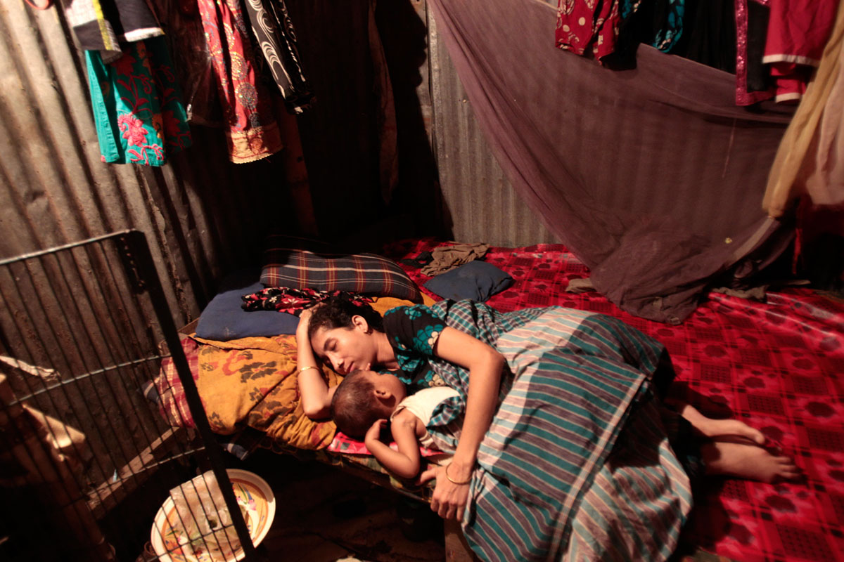 Bangladesi textilgyári munkás pihen az otthonául szolgáló kunyhóban egy nyomornegyedben