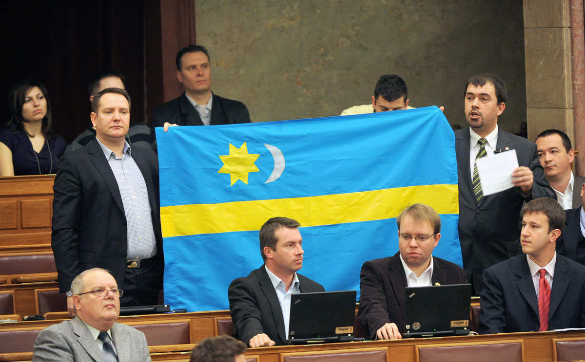 Szávay István jobbikos képviselő, Suhajda Krisztián képviselőtársa segítségével egy székely zászlót emel fel, miközben Mindannyian székelyek vagyunk címmel felszólal az Országgyűlés tegnapi plenáris ülésén