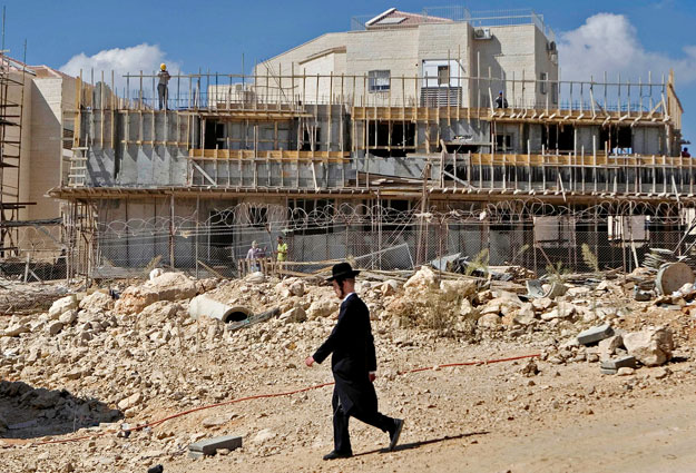 Épülő ház mellett megy el egy ultraortodox zsidó férfi a ciszjordániai Beitar Illitben lévő zsidó telepen