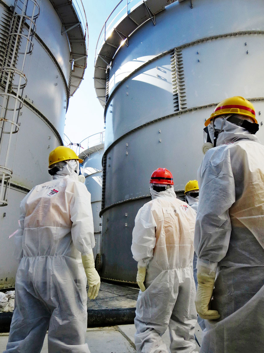 A japán ipari és gazdasági miniszter, Motegi Tosimicu (középen) és kísérete sugárszennyezett víztartályokat ellenőriz a megrongálódott fukusimai atomerőműnél