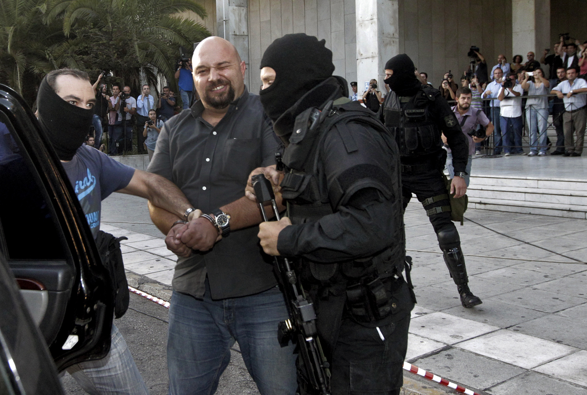 Az Arany Hajnal egyik letartóztatott parlamenti képviselője a kamerák felé kaccsint az athéni rendőr-főkapitányság előtt