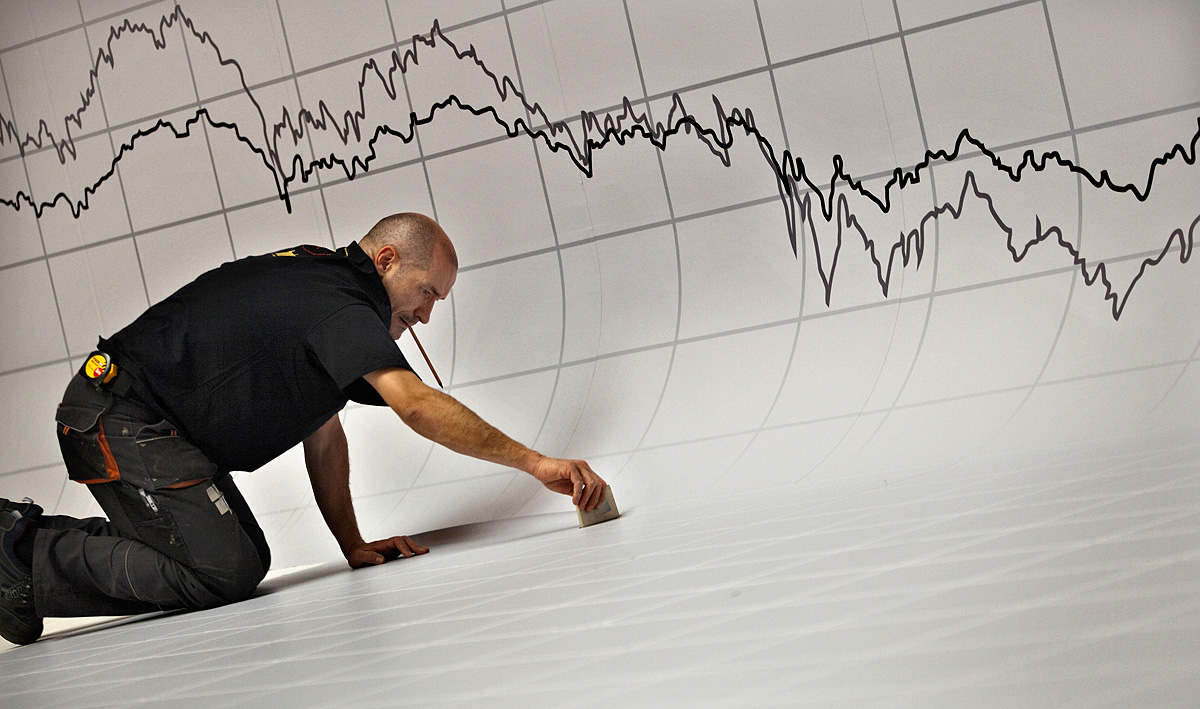 A graph is seen above a worker as he puts the finishing touches to a stage decoration for an investment funds awards dinner at the Madrid stock exchange May 17, 2012. Spain's benchmark IBEX index fell nearly 2 percent to its lowest level since mid-20