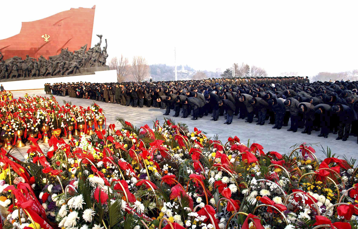 A szobrot ellepő virágok előtt hajlonganak a Kim Dzsong Ilre emlékező észak-koreaiak