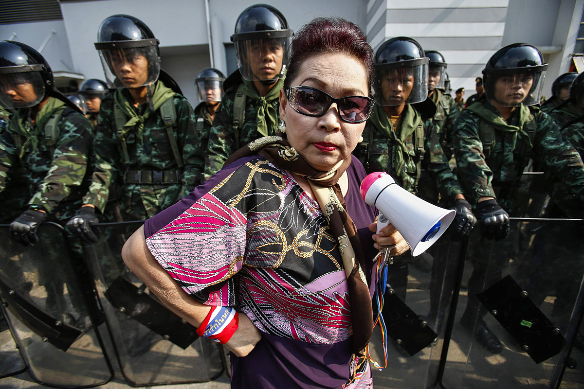 Egy kormányellenes tüntető áll a bangkoki védelmi minisztérium előtt. Az épületet katonák védik, ugyanis itt rendezte be átmeneti irodáját Jinglak Sinavatra miniszterelnök