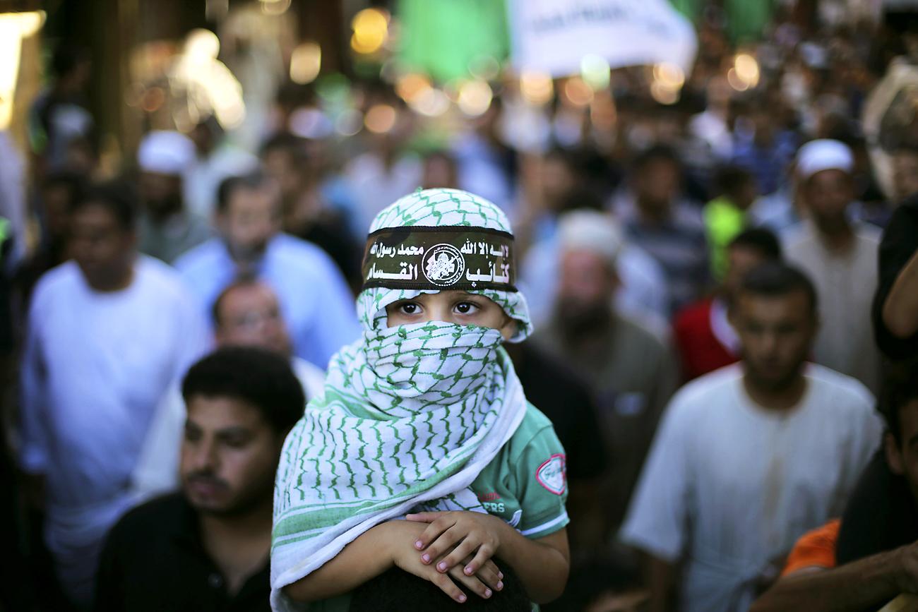 Palesztin fiú a Hamássz katonai szárnyának, az ezzedin al-Kasszam Brigádoknak a sapkájában