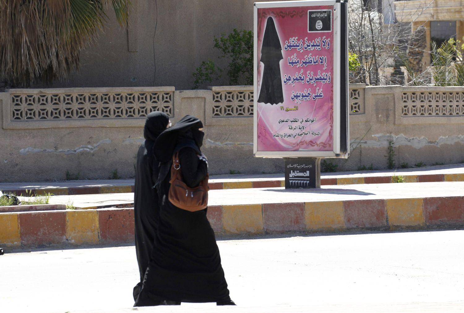 Nők egy helyes öltözködésre figyelmeztető transzparens mellett az Iszlám Állam de facto fővárosában, a szíriai Rakkában