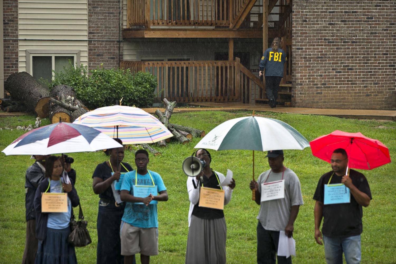 Egy FBI-ügynök jár házról házra a Brown-család lakása környékén, miközben civilek tiltakoznak a fiú halála miatt