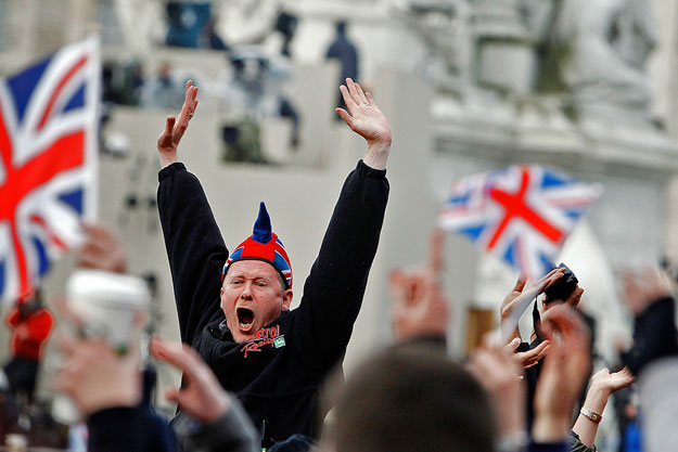 A Buckingham Palotával szemközti hatalmas szobor lábánál várják a 'rajongók' a királyi család tagjait