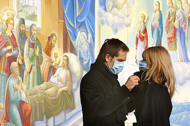 Védőmaszkot viselő pár beszélget egy betegágyon fekvő férfit ábrázoló freskó mellett a kijevi Mihajlovszkij-székesegyházban