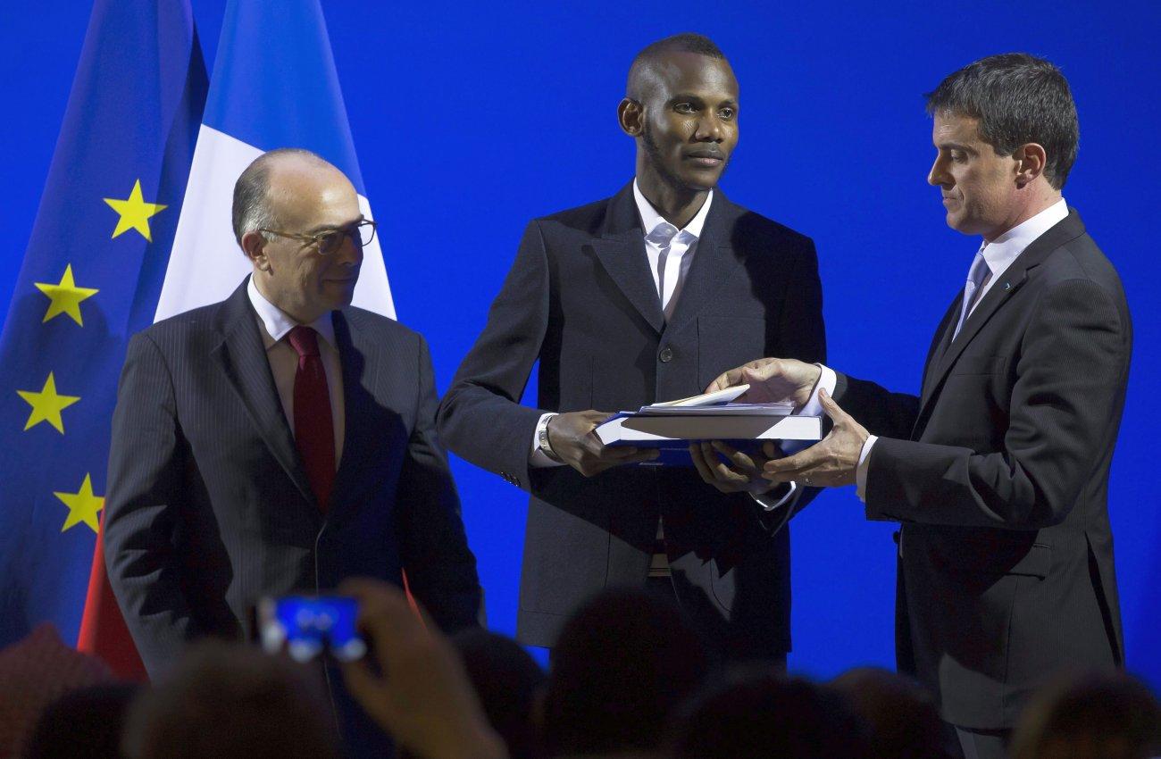 Manuel Valls kormányfő (j) átadja a kitüntetést és a francia állampolgársági okmányt Lassana Bathilynak