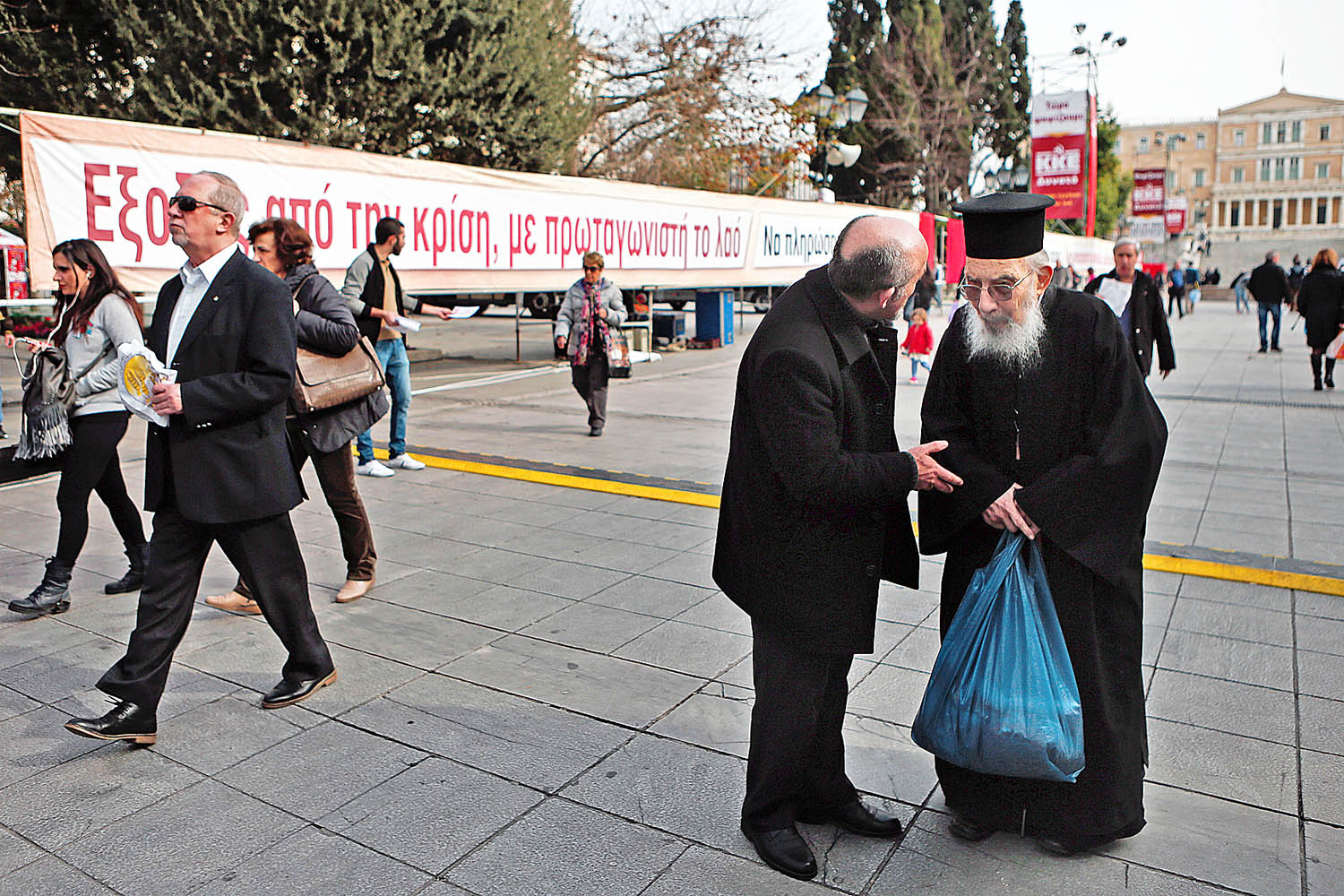 Ortodox pap beszélget egy athéni járókelővel a kommunisták plakátja előtt