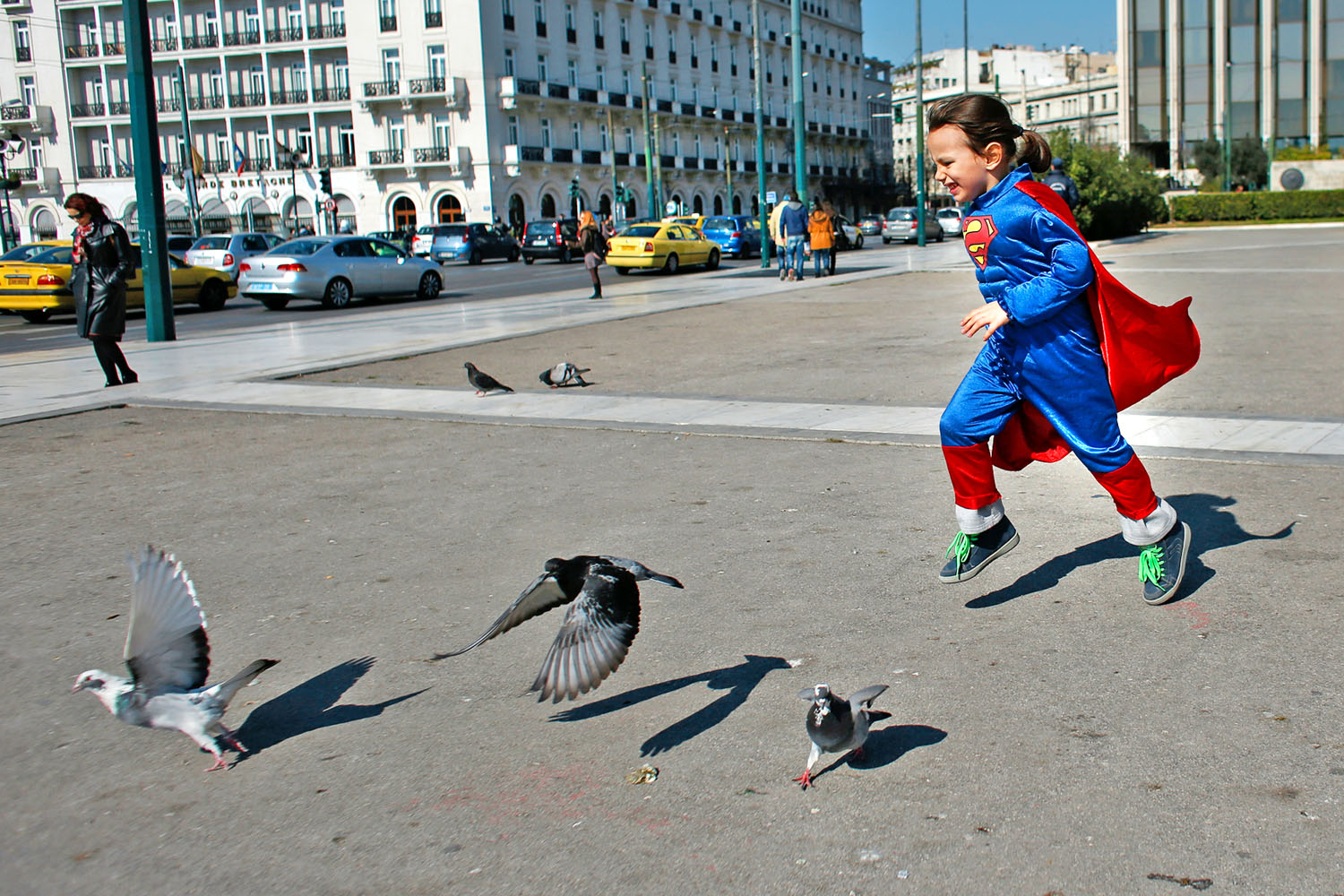 Superman-jelmezes kisgyermek galambokkal játszik Athénban. Óvatosnak kell lenni