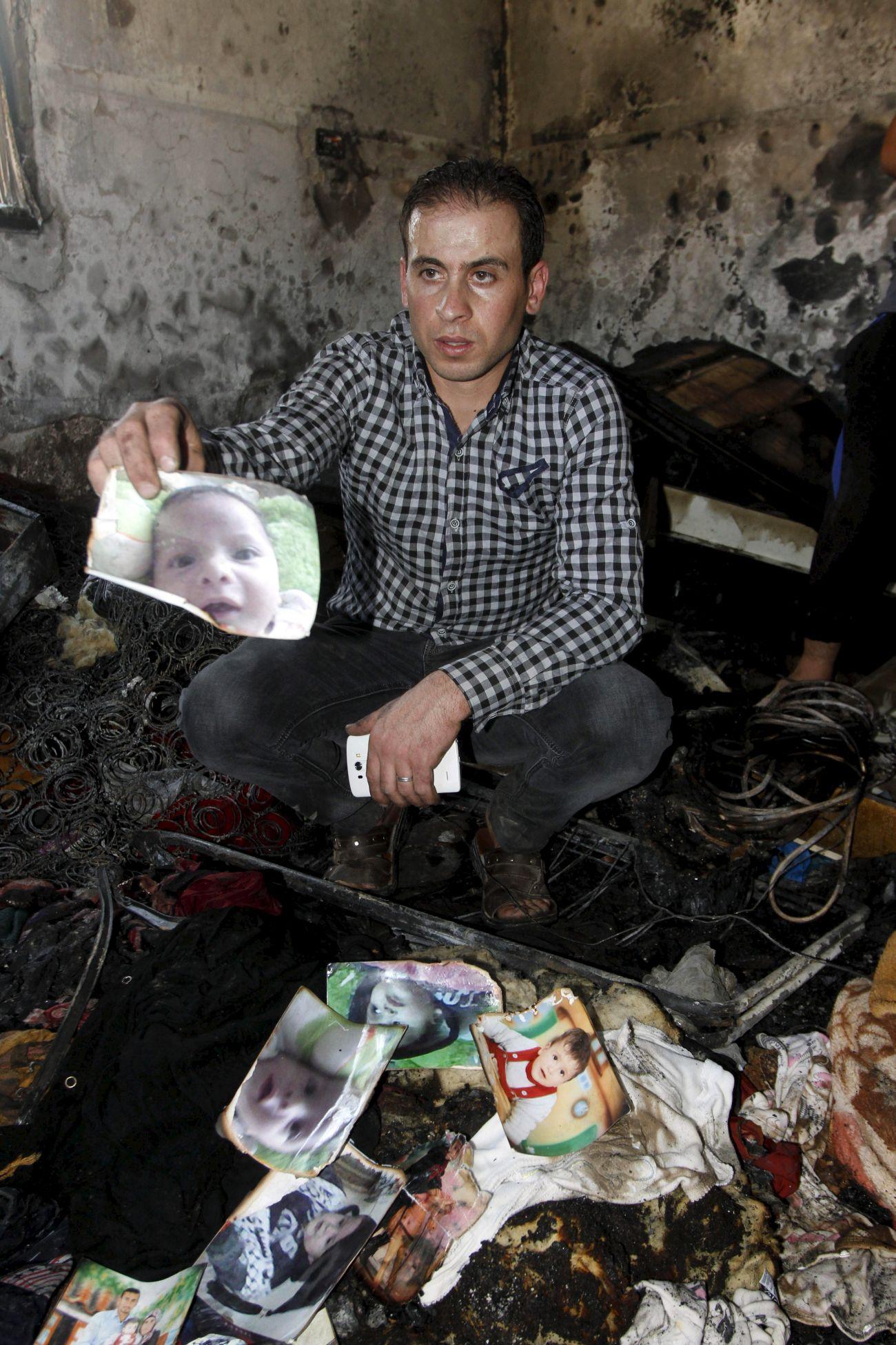 Családtag az üszkös romok között a 18 hónaposan halálra égett kisfiú, Ali Szaad Davabsa arcképével