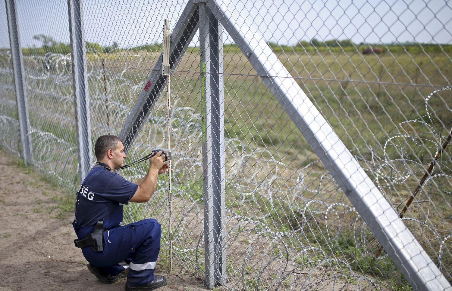 Rendőr méricskéli a kerítésen vágott lyukat Ásotthalomnál