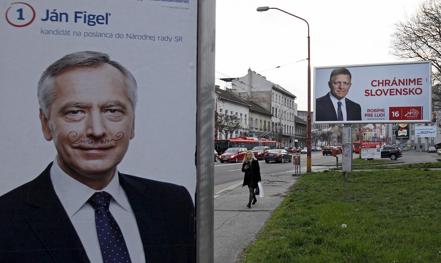 Figel bajusszal. Hátul a SMER-SD plakátja Robert Ficoval. Megvédené Szlovákiát
