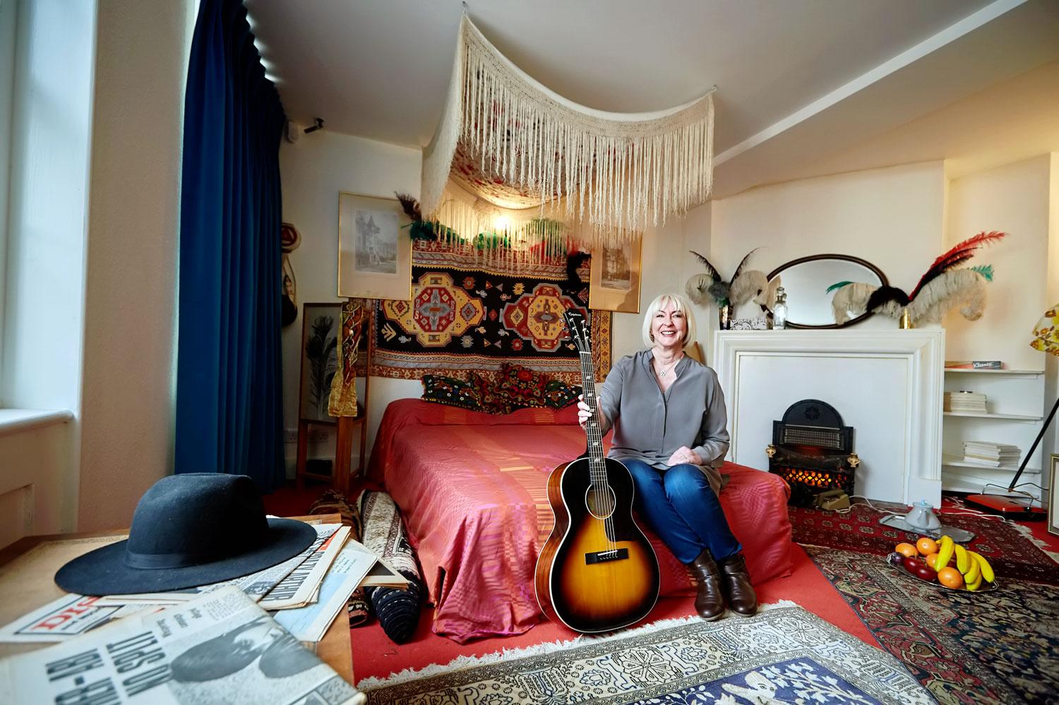 Jimi Hendrix barátnője, Kathy Etchingham a múzeummá alakított közös lakásukban, kezében a zenész Epiphone FT-79-es gitárjával