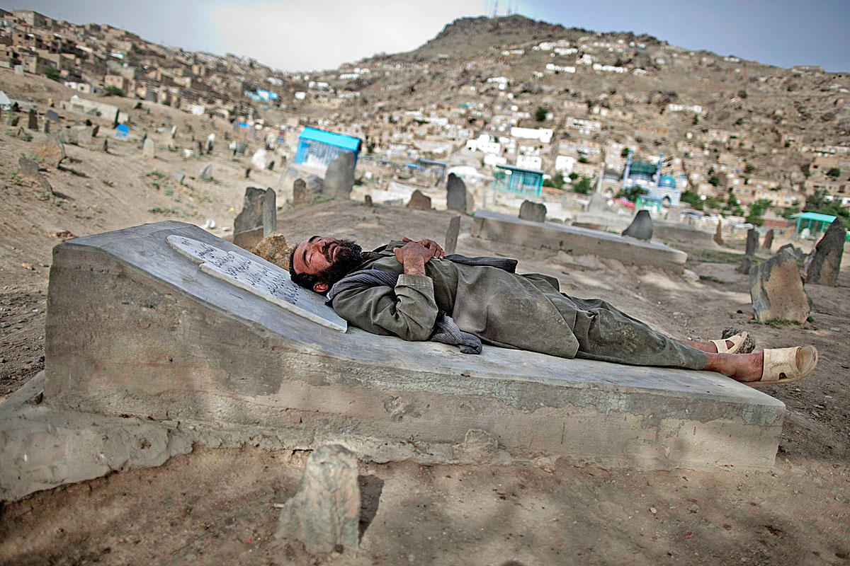Afgán férfi alszik egy temető sírkövén Kabulban