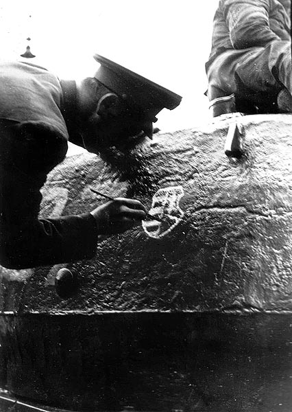 Egy köpenyes katonatiszt Kossuth-címert pingál a tankjára
