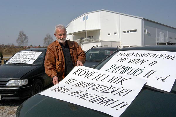 Zacher Emil feliratokat helyez el a tiltakozók kocsiján, háttérben az új jégcsarnok