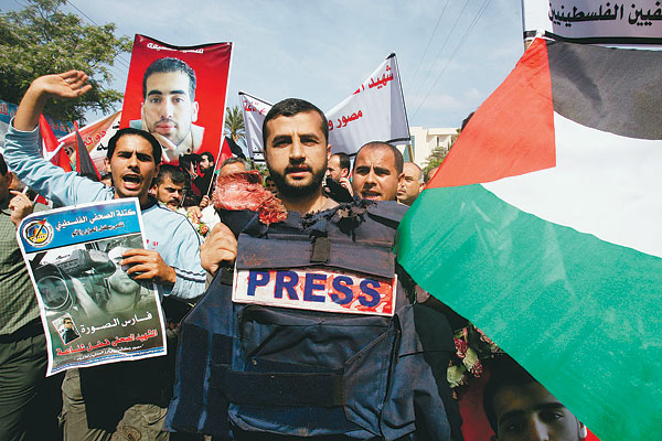 Izraeli repesz által megölt Reuters-operatőr mellényét mutatja a kamerának egy gyászoló Gázában