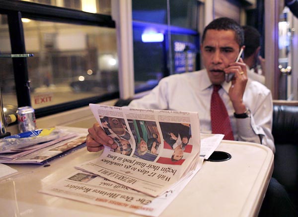 Barack Obama a többi elnökjelölt fotójával illusztrált lapot olvas kampánybuszán