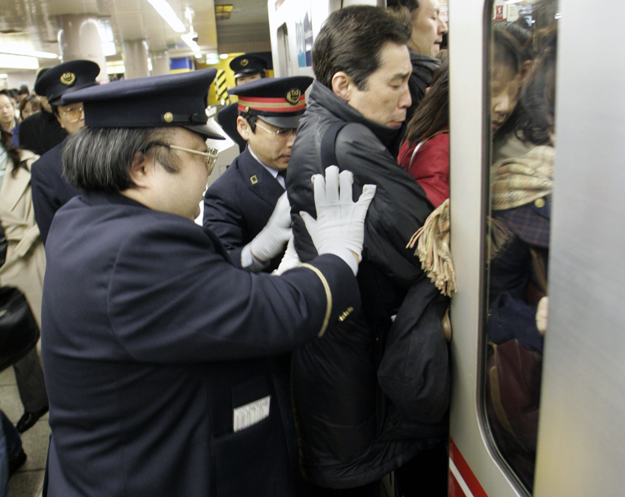 Peronőrök passzírozzák be az utolsó utasokat is a zsúfolt tokiói metróba az Ikebukuro állomáson