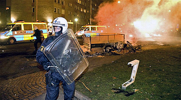 A riot police officer stands guard while colleagues extinguish burning barricades on the main road in the heavily-immigrant populated neighborhood of Rosengaard of the southern Swedish city of Malmoe on December 19, 2008. Some 100 youths rioted in la