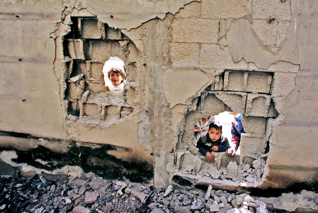 Palesztin gyerekek néznek be egy gázai kórház lövedék ütötte falán