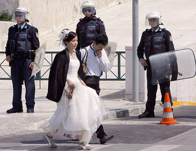 Frissen házasodott japán turisták mennek el rohamrendőrök előtt Athénban