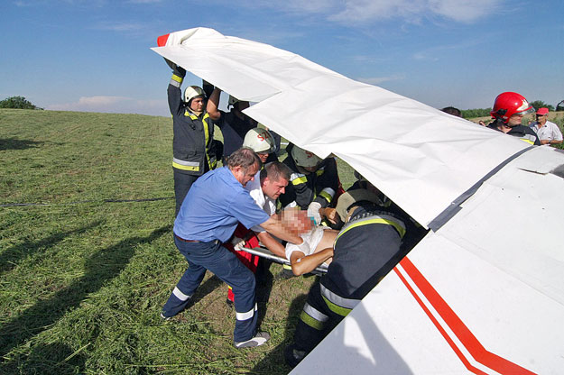 Tűzoltók és mentők emelnek ki egy férfit egy összeroncsolódott motoros kisrepülőgépből, amely előzőleg oktatórepülés közben kényszerleszállást hajtott végre, majd légörvénybe került és a földhöz csapódott