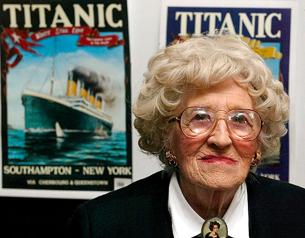 Millvina Dean, a Titanic katasztrófájának utolsó túlélője, amint az elsüllyedhetetlennek tartott luxusgőzöst ábrázoló korabeli plakátok előtt ül. Dean 1912. április 10-én kilenchetes csecsemőként indult el szüleivel és bátyjával a végzetes útra