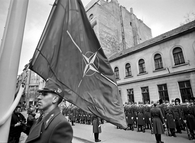 Legalább a tűzfalat egy pillanatra eltakarja… Felvonják a hivatalos NATO-zászlót a Honvédelmi Minisztérium főbejárata előtt