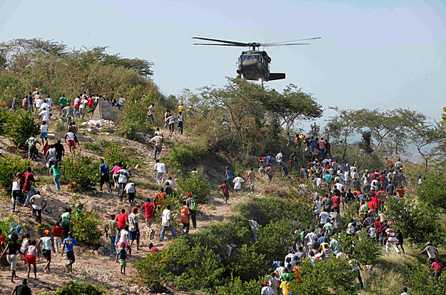 Az emberek egy amerikai katonai helikopter felé futnak, amely ivóvizet dob le Port-au-Prince-ben
