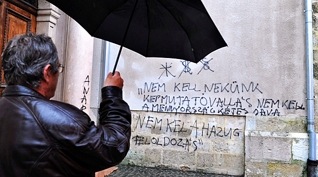 Egy férfi áll a győri bazilikánál, amelynek falán anarchista szövegekkel összefirkálták
