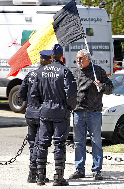 Belga zászlót vivő férfival beszélgetnek rendőrök a brüsszeli királyi palota előtt