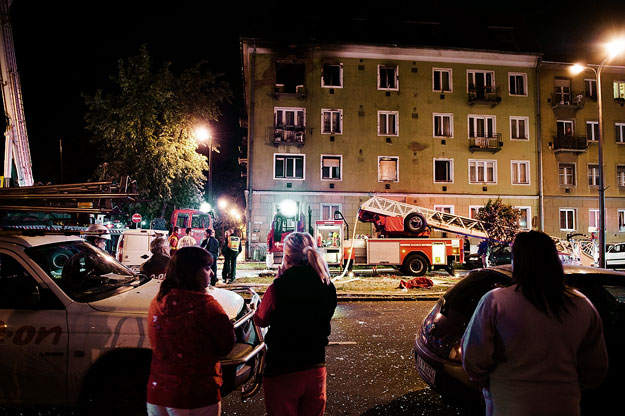 Lakók nézik az utcán, amint tűzoltók dolgoznak az éjjeli órákban Nyíregyházán
