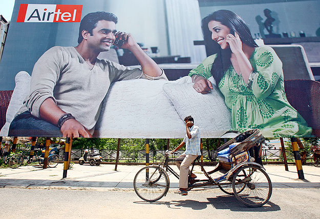 A rickshaw driver talks on his mobile phone as he rides past a billboard outside a railway station in the northern Indian city of Chandigarh May 26, 2009. India's Bharti Airtel, which has restarted merger talks with South Africa's MTN Group, said on 