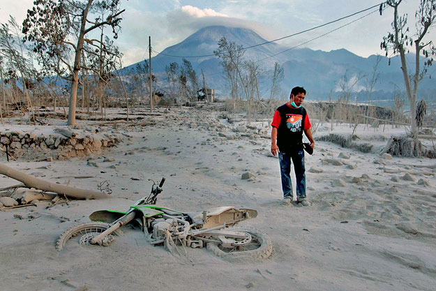 A villager stands in front of Mount Merapi,  near his motorcycle covered by ash at Kaliadem village in Sleman, near the ancient city of Yogyakarta, October 27, 2010. One of Indonesia's most active volcanoes spewed out clouds of ash and jets of searin