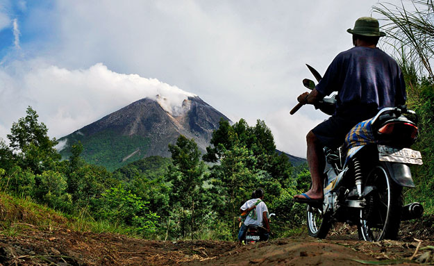 Villagers ride on motorcycles as Mount Merapi volcano emits smoke from Cangkringan village October 25, 2010. Indonesia Volcanology and Geological Disaster Mitigation Center issued a high alert status warning for the volcano on Monday, according to lo