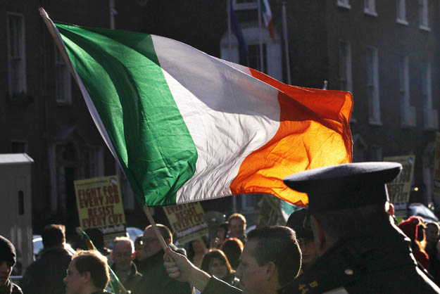 A protestor waves a tri-color flag outside Government Buildings in Dublin November 24, 2010. Ireland set out its four-year plan on Wednesday to make 15 billion euros in savings by 2014 to bring down its record deficit.  REUTERS/Cathal McNaughton (Ire